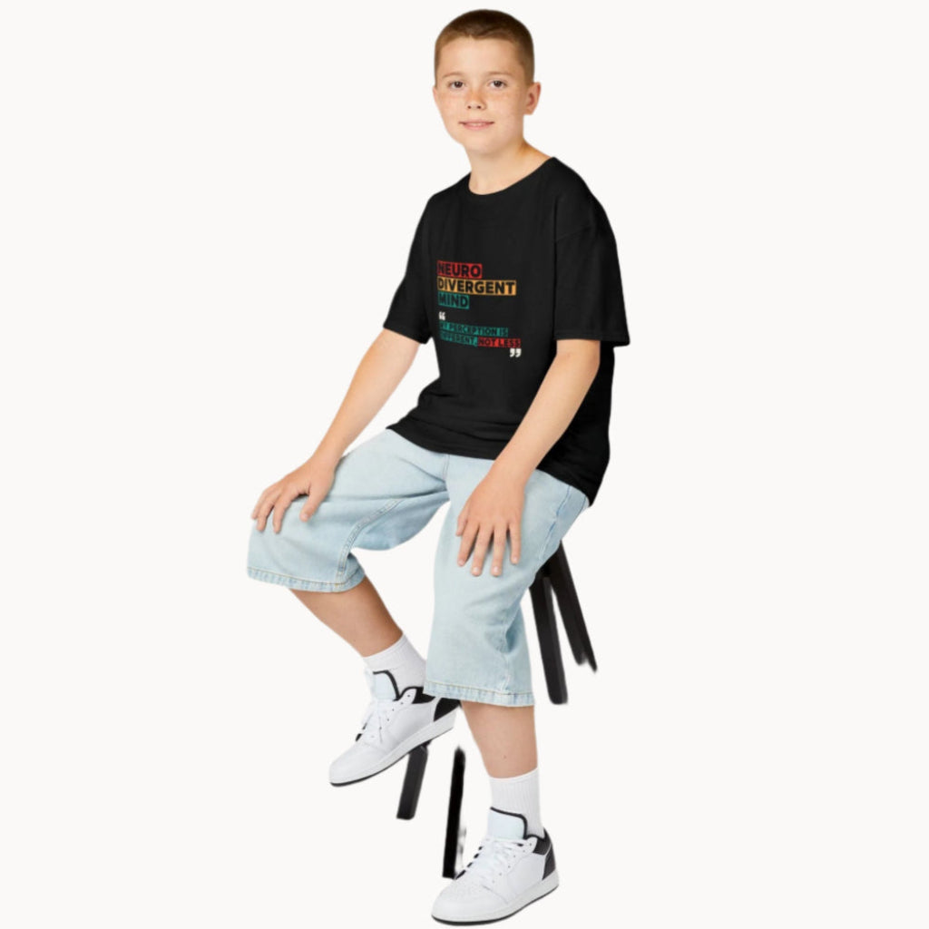 Boy sitting on a stool in a black oversized t shirt with words Neurodivergent Mind My perception is different, not less on front highlighted in red, yellow and green